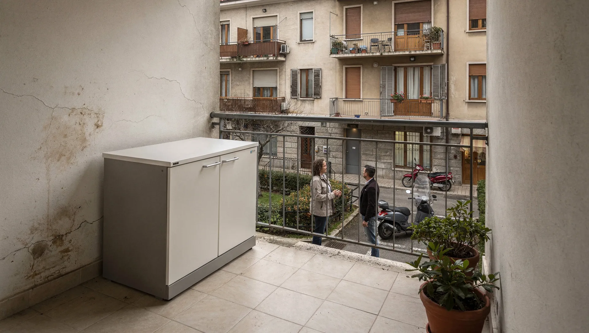 Balcone di un condominio con armadio da esterno visibile sulla facciata e residenti che discutono nel cortile